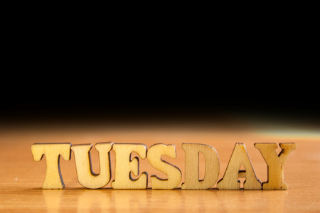 The word 'tuesday' made of wooden letters. wood inscription on table and dark black backgroundの写真素材
