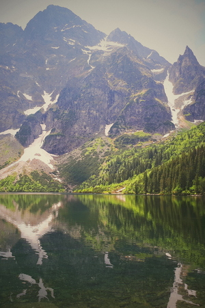 A beautiful landscape at the Morskie Oko in the polish Tatras. The water mirror reflects the mountains in many colors, green and white. Snow on the rocks.の写真素材