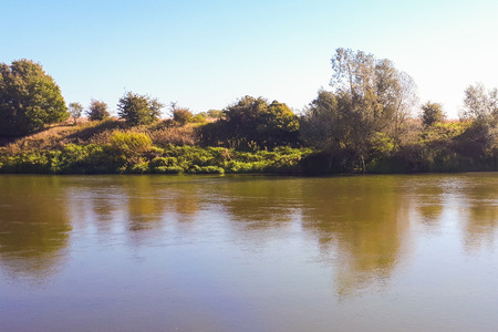 Flowing river in the autumn season. The water mirror reflects the plants growing by the river bank....