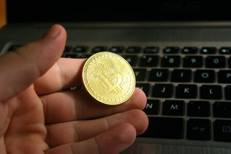 Bitcoin coin in hand. Laptop blur background. Digital crypto currency financial conceptの写真素材