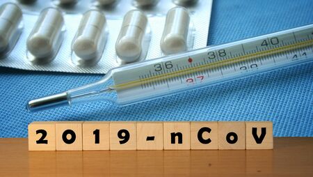 coronavirus covid-19 and thermometer in background. Wooden blocks with inscription 2019-nCov....