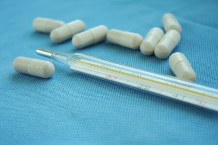 Mercury thermometer with tablets on blue background. Instruments necessary for cold and flu....