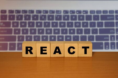 REACT message word on a wooden desk on cube blocks with a laptop keyboard  background
の写真素材