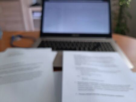 Paper sheets and documents lying on the table, and in the background a modern laptop. Defocused...