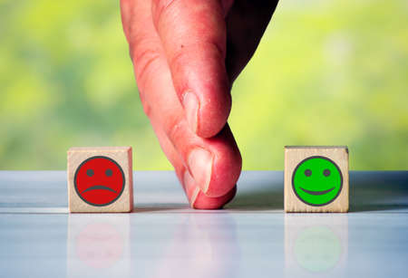 The hand separates two wooden blocki with red sad face and green happy face. Symbol for the differenceの写真素材