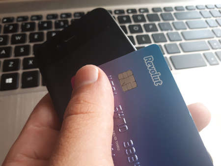 Revolut card logo and smartphone in hand on laptop keyboard background on circa October 2019,...