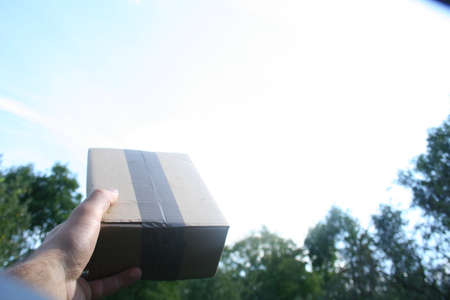 A courier package that has just arrived at the addressee as a gift held in hand against the sky