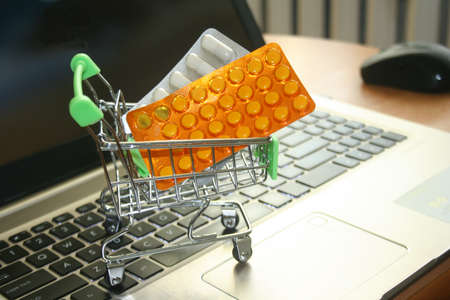 variety of pills in a supermarket trolley on a laptop backgroundの写真素材