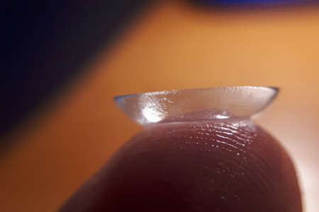 Contact lense on finger tip, macro. Contact lenses macro close up. Man holding lens on finger. Customer, patient or eye doctor, oculist or optician in clinic.の写真素材