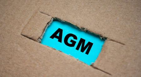 A cut-out hole in the paper cardboard, and under it a piece of paper with the word AGM. The word AGM conceptの写真素材