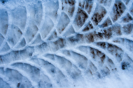 Diagonal traces of car tires in the snow on the asphalt. Close up view from above. Asphalt covered...