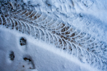 Diagonal traces of car tires in the snow on the asphalt. Close up view from above. Asphalt covered snow. Dangerous road condition. Tire trial on ice in winter season.の写真素材