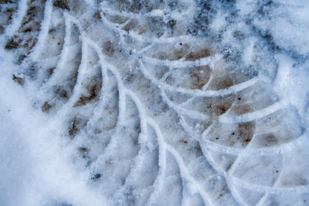 Diagonal traces of car tires in the snow on the asphalt. Close up view from above. Asphalt covered...