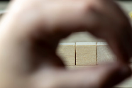 A hand forms a circle around two wooden cubes on a table focusing attention on the objects. This...