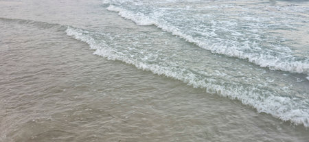 Gentle waves lapping on a sandy beach create a serene coastal scene. The calm water reflects soft...