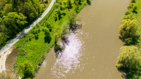 Aerial view of a tranquil river surrounded by lush green trees and a winding road. The serene...