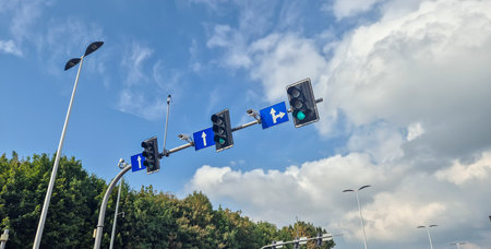 Rzeszow Poland - September 15 2025: A traffic light displaying green signals for straight and left turns on a busy road with blue sky and clouds in the background.のeditorial素材