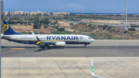 Alicante Spain - July 17 2025: A Ryanair airplane taxies on the runway with a clear blue sky and coastal background showcasing modern air travel in an urban setting.のeditorial素材
