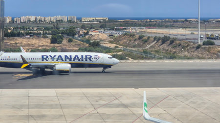 Alicante Spain - July 17 2025: Ryanair airplane taxiing on the runway with the Mediterranean Sea in the background showcasing summer travel atmosphere.のeditorial素材