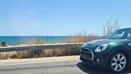 A sleek green car parked by a beachside road with a clear blue ocean in the background. Ideal for showcasing travel leisure and automotive themes in sunny weather.の写真素材