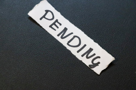 A close-up view of a torn paper label with the word PENDING written in bold letters on a dark textured background symbolizing wait or delay in various contexts.の写真素材