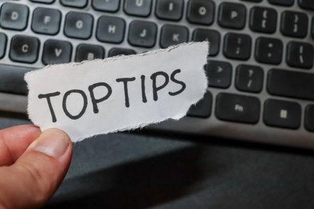 Close-up of a hand holding a torn paper with the words TOP TIPS against a blurred keyboard background. Ideal for articles on advice or guidance.の写真素材