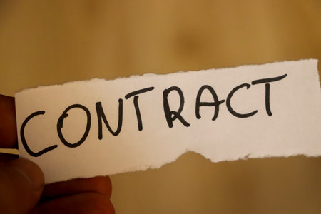 A close-up view of a hand holding a torn piece of paper with the word CONTRACT written in bold letters. The background is blurred suggesting a professional setting.の写真素材