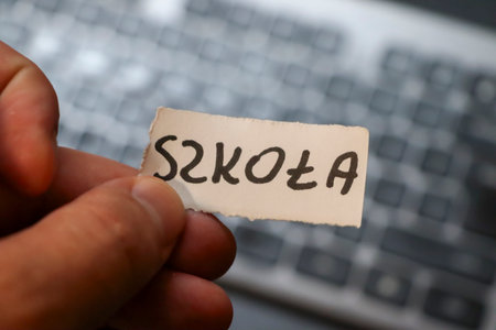 A hand holding a piece of paper with the word Szkola which means school in Polish. The background features a blurred keyboard emphasizing education and technology.の写真素材