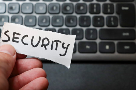 A person holding a torn piece of paper with the word SECURITY against a blurred computer keyboard background symbolizing cybersecurity awareness and protection.の写真素材