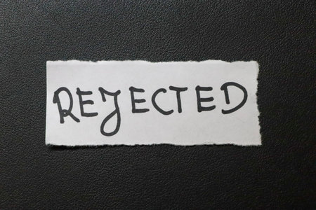 A torn paper note with the word REJECTED written in bold creative font placed against a dark textured background. Reflects themes of rejection and disappointment.の写真素材