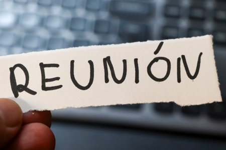 A hand holding a piece of paper with the word Reunion written in bold. The background features a blurred keyboard symbolizing communication and connections.の写真素材