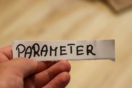 A hand holds a piece of paper with the word PARAMETER handwritten showcasing a clear concise message. The background is softly blurred focusing on the texts significance.の写真素材