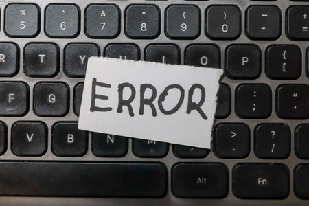 A close-up view of a black keyboard with a paper note labeled ERROR placed on the keys symbolizing computer issues or technological problems in an office environment.の写真素材