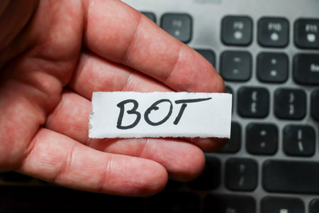 Hand holding a small paper with the word BOT written in black ink positioned above a laptop...