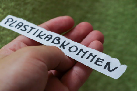 A hand holding a torn paper strip with the handwritten word PLASTIKABKOMMEN visible against a soft green background symbolizing recycling and environmental awareness.の写真素材