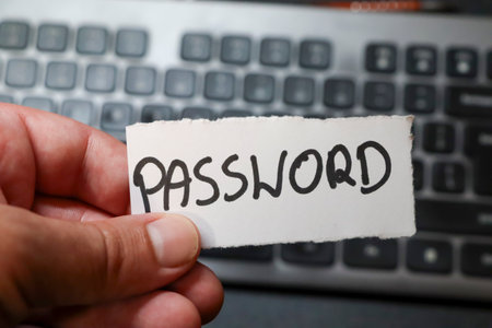 A hand holding a note with the word PASSWORD against a background of a computer keyboard emphasizing security and digital privacy in modern technology.の写真素材