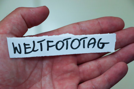 Hand holding a paper strip with the handwritten word WELTFOTOTAG symbolizing World Photography Day....