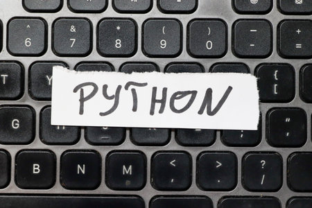 Handwritten word PYTHON on a piece of paper placed on a black keyboard symbolizing programming and computer science. Suitable for tech-related projects.の写真素材