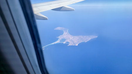 Aerial view from an airplane window showing a scenic island surrounded by clear blue waters taking a flight towards a summer destination evoking a sense of adventure and exploration.の写真素材