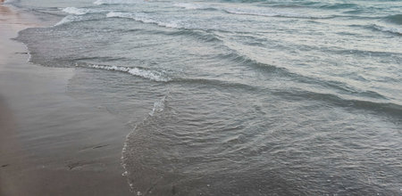 Gentle waves lap against a serene beach at dusk creating a calm and peaceful atmosphere. The smooth...