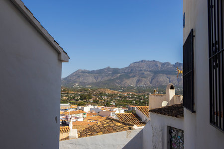 A panoramic view from a narrow street in Altea Spain showcasing traditional whitewashed buildings and the scenic mountains in the background. Clear blue sky enhances the vibrant landscape.の写真素材