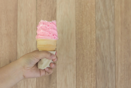 Ice cream strawberry cone held up to the hot summer on wood backgroundの写真素材