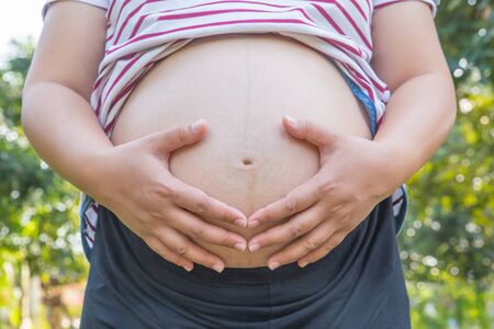 Pregnant Woman Holding her Hands in a Heart Shape on her Baby Bump. Pregnant Belly with Heart Symbol. Maternity Conceptの写真素材