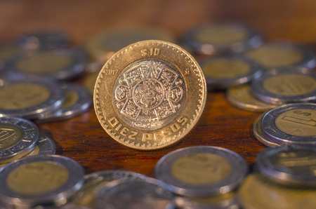 Mexican Coin in the middle of other coins in a table of woodの写真素材