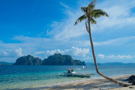 Tropical landscape with mountain islands, palm tree and lonely boatの写真素材