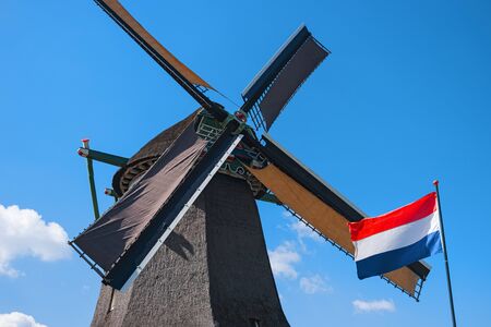 Old windmill and waving flag, Zaanse Schans, Netherlands. Typical dutch mill. Rural landscape. Symbol of the Netherlandsの写真素材