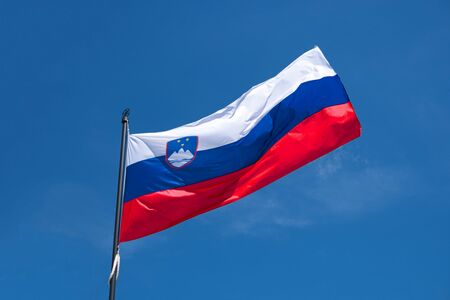 Flag of Slovenia on flagpole waving in the wind. Slovenian national official flag on blue sky background. Patriotic symbol, bannerの写真素材