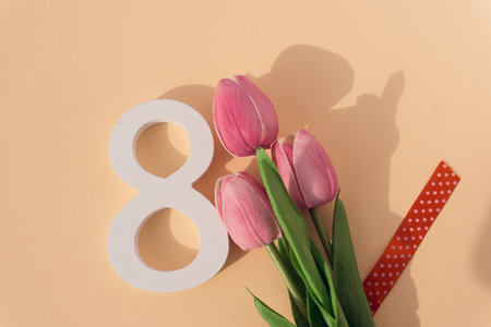 top view of bouquet of pink tulips and red ribbon on beige backgroundの写真素材