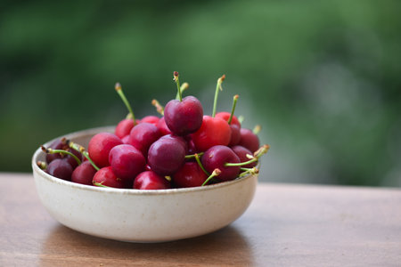 Fresh cherries in a bowl on a wooden table with blurred backgroundの写真素材