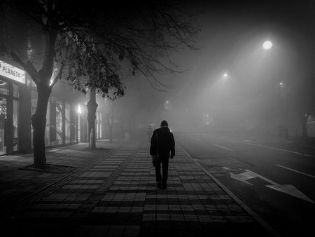 Man walking alone in a foggy street at night, monochromeの写真素材